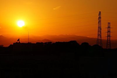 Silhouette electricity pylon against orange sky