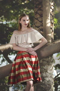 Young woman looking away while standing against tree in park