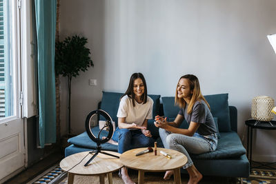 Smiling young female influencers with beauty product vlogging at home