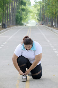 Full length of overweight woman tying shoelace on footpath