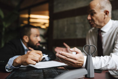 Senior male lawyer discussing over contract with colleague at desk in office