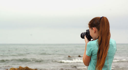 Woman photographing at beach against sky
