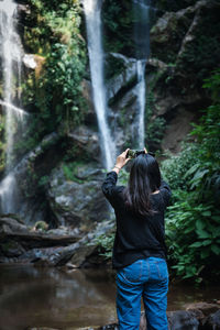 Rear view of man standing against waterfall in forest