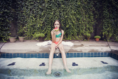 Girl eating watermelon slice while resting at poolside