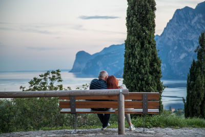 Rear view of man sitting on bench against sea