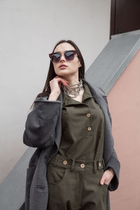 Cropped front view postttait of young woman in grey coat and suit against wall outdoors, outwear 