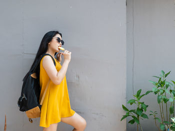 Young woman looking away while standing against wall