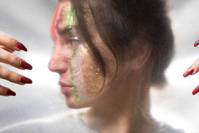 Close-up of woman with glitter on face seen through glass