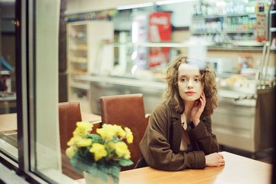 Portrait of young woman looking down while sitting on window