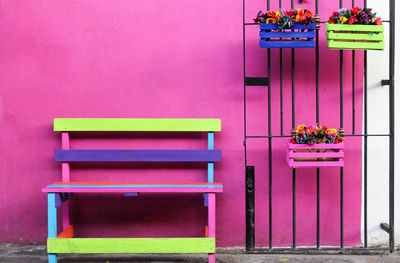 Colorful bench by potted plants on gate against wall