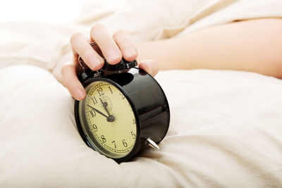 Cropped hand holding alarm clock on bed