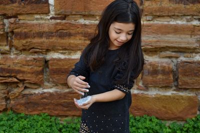 Girl holding powder paint while standing against brick wall