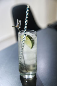 Close-up of glass on table with gin and tonic, a slice of lime, ice, stirrer and straw