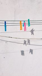 Close-up of multi colored clothespins hanging on rope against wall
