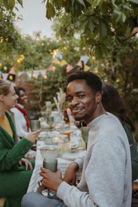 Side view portrait of smiling young man enjoying with friends at dinner party in back yard