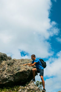 Low angle view of man standing on rock against sky