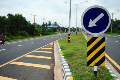 Road sign by street against sky in city