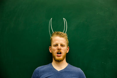 Portrait of young man with horned tattoo on blackboard