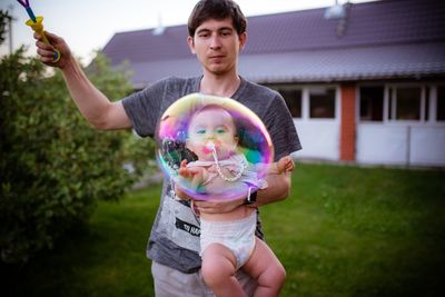 Man holding daughter seen through bubble in yard