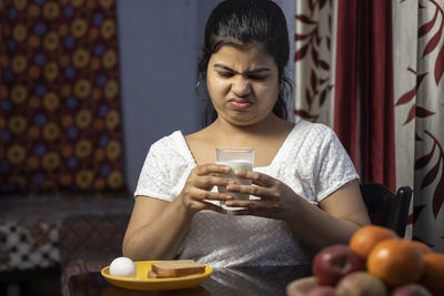 An indian asian woman holding a glass of milk and showing unhappy face in a domestic room