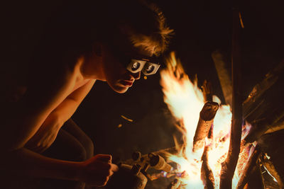 Shirtless young man preparing fire at night