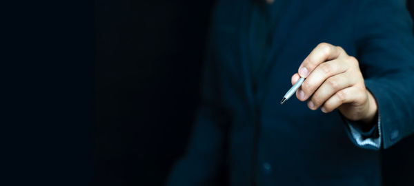Midsection of businessman gesturing against black background