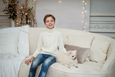 Handsome little caucasian boy on the sofa with white dog on