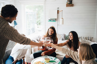 Male and female friends toasting wineglasses over food at table in cottage