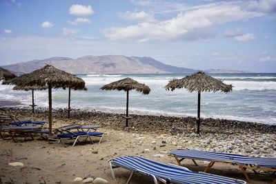 Deck chairs on beach against sky