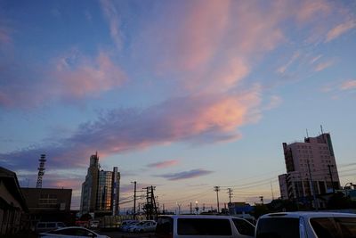 Cars on road by buildings against sky during sunset