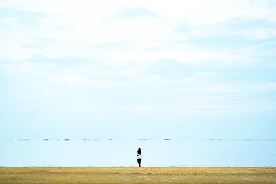 Rear view of woman standing by sea against sky