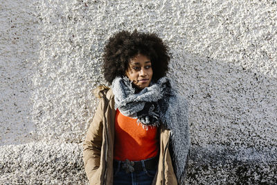 Afro young woman with hands in pockets against textured wall