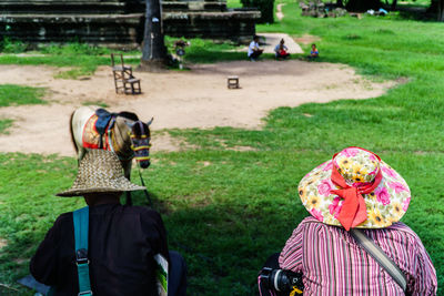 Rear view of people in sun hat with horse on field