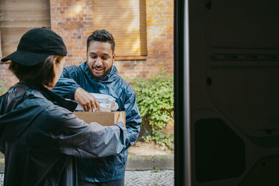 Male and female delivery coworkers assisting each other while holding parcels