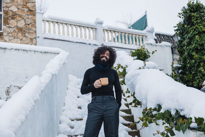 Smiling bearded man with coffee cup standing on snow covered steps