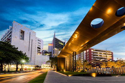 Illuminated street amidst buildings against sky at dusk