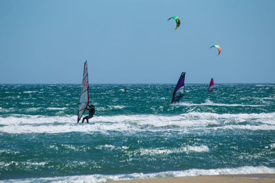 People kiteboarding and windsurfing against clear sky