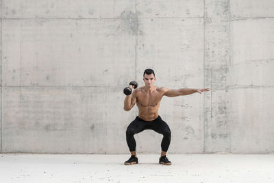 Full length of shirtless man with arms raised against wall