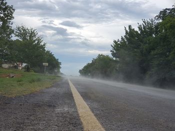 Empty road by trees against sky