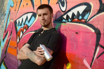 Portrait of young man standing against graffiti wall