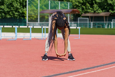 Fit african american woman enjoys stretching body standing on red track of city stadium near park