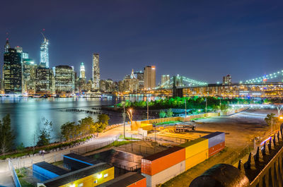 Illuminated buildings by river against sky in city at night