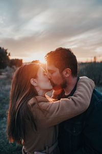 Young couple kissing against sky during sunset