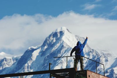 Man with arms raised standing on observation point by snowcapped mountains