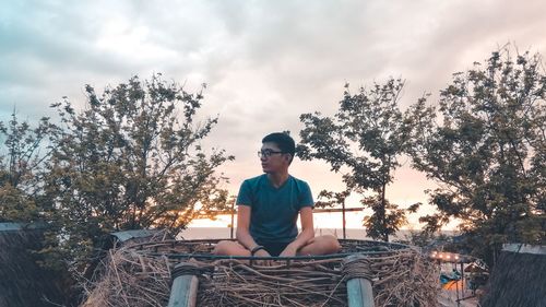 Full length of man sitting on sticks and dry grass against sky