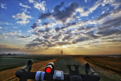 Road amidst field against sky during sunset