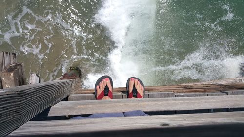 View of pier and womans feet in red flip flops sticking out over  ocean water