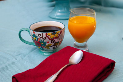 Black coffee in a colorful flower print cup with orange juice on a blue table cloth