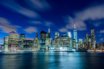 Illuminated skyscrapers by east river against sky at night