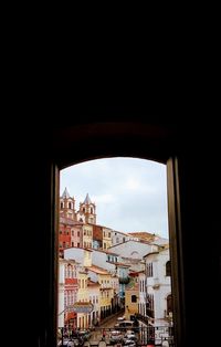 Buildings in city against sky seen through window